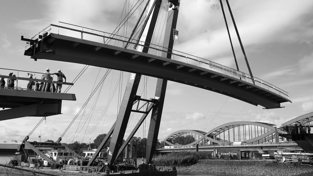 Workers lifting a bridge section with a crane